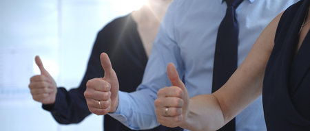 Business people team showing thumbs up gestures in a row, expressing approval, agreement, success, and full support for a project or strategy in a corporate office setting with sun flairの写真素材
