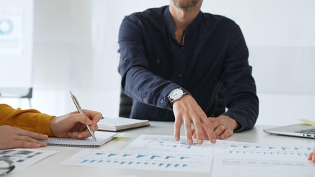 Professional colleagues reviewing financial charts, collaborating on strategic planning, gesturing toward data visualizations during corporate meeting in contemporary workspaceの写真素材