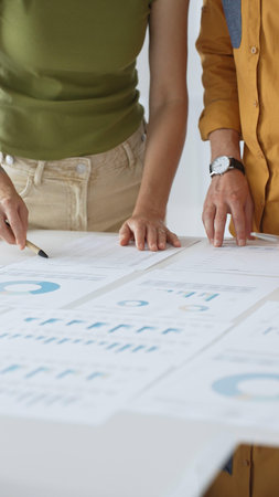 Business professionals analyzing financial reports, pointing at charts during collaborative meeting, discussing data with focused professional demeanorの写真素材