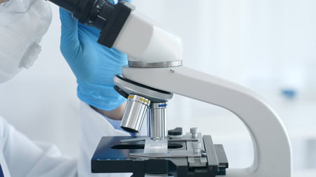 Microscope and scientists hands in blue gloves adjusting close up in laboratory set. Medicine,...
