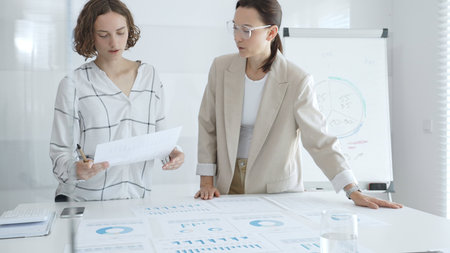 Two businesswomen analyzing financial reports and discussing growth strategies while collaborating...