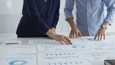 Professional business team analyzing financial reports, sharing insights and planning strategic decisions in modern workplace settingの写真素材