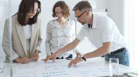 Business team collaborating on financial data analysis, pointing at charts and graphs spread out on a light table during a corporate meeting. Business people conceptの写真素材