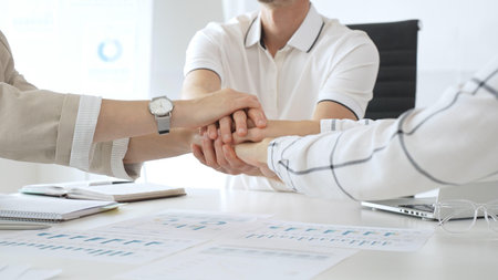 Business people team joining hands over workplace documents, symbolizing collaborative spirit and...