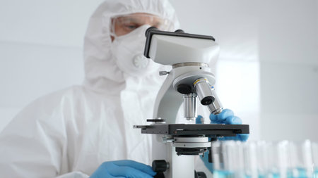 Male scientific researcher or virologist wearing protective gear adjusting microscope, analyzing lab...