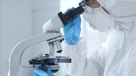 Medical virologist in a hazmat suit, mask, and gloves, diligently working at a microscope in a...