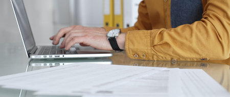 Man working on laptop, typing on keyboard in office, managing business documents and modern...
