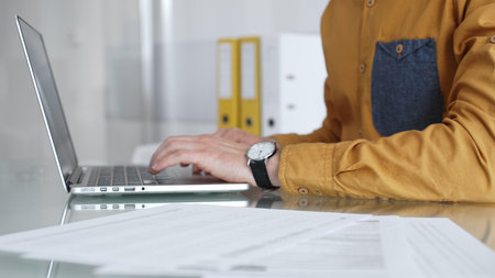 Man working on laptop, typing on keyboard in office, managing business documents and modern...