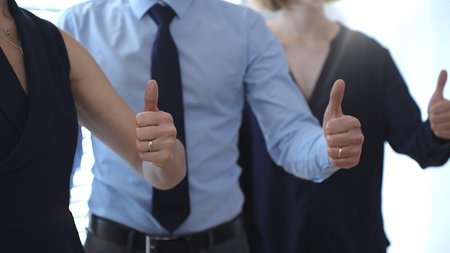 Business people team showing thumbs up gestures in a row, expressing approval, agreement, success, and full support for a project or strategy in a corporate office setting with sun flairの写真素材