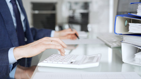 Accountant working in office, calculating finance data using black calculator and taking notes for budget planning. Audit and taxes in businessの写真素材