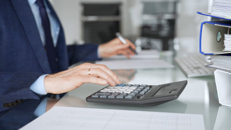 Accountants hands calculating and writing on financial documents at a desk, managing budgets, reports and tax paperwork. Audit and taxes in businessの写真素材