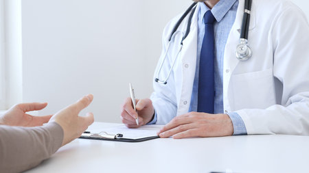 Doctor man taking notes while listening to a female patient explaining her symptoms during a medical consultation in the clinic office. Medicine and health care conceptの写真素材