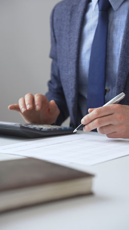 Professional accountant calculating expenses, documenting financial details on notepad while working at corporate desk. Audit and taxes in businessの写真素材