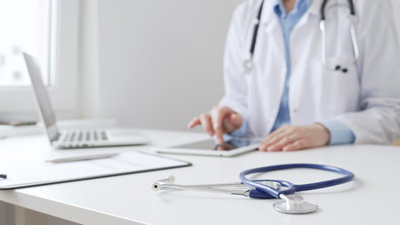 Closeup of blue stethoscope is lying on the table near female doctor using a digital tablet and patient chart on the desk in a modern medical office, representing healthcare technology. Medicineの写真素材