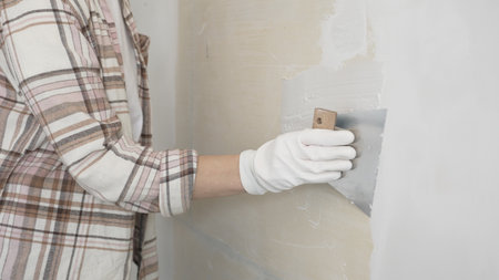 Unknown female construction worker wearing protective gloves applying plaster, smoothing wall surface during home renovation workの写真素材