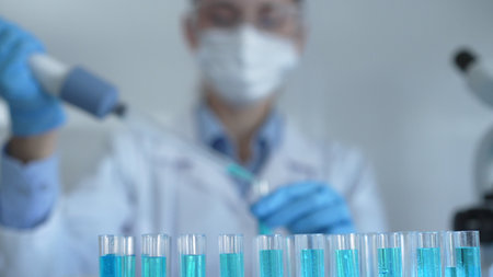Laboratory tubes are in focus, closeup view. Female scientist researcher is using a micropipette at...