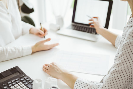 Two accountants using a laptop computer for counting taxes at white desk in office. Business Woman pointing into screen with a pen. Teamwork in business audit and financeの写真素材