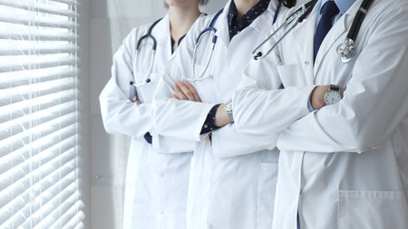 A team of doctors in white lab coats standing with arms crossed demonstrates experience, unity, and the essence of medicine in a modern clinicの写真素材