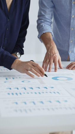 Professional team collaborating, reviewing financial graphs, calculating metrics, discussing...