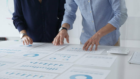 Business professionals analyzing financial charts, gesturing over spreadsheets during collaborative meeting in contemporary workspace, discussing data driven insightsの写真素材