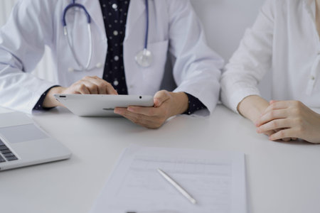 Doctor and a patient. The female physician, wearing a white medical coat over a dark blue dotted...