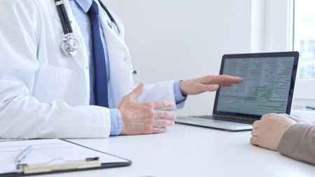 Doctor reviewing digital test results with patient, discussing health findings on laptop screen during clinical consultation. Medicine and health care concept.の写真素材