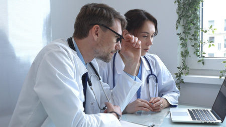 Two doctors are studying medical charts on a laptop, discussing patient data in a hospital or clinical setting. Medicine and healthcare concept.の写真素材