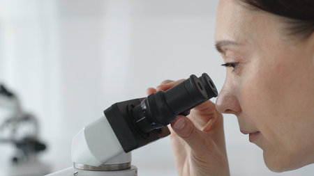 Female scientist peering into microscope, analyzing biological sample with precision in sterile...