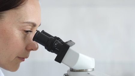 Female scientist peering into microscope, analyzing biological sample with precision in sterile laboratory research environment. Medicine and science conceptの写真素材