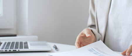 Businesswoman analyzing financial reports, reviewing charts on laptop and paper documents while...