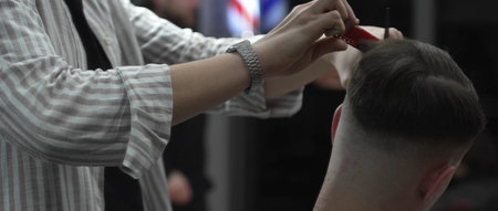 Skilled barber trimming customers hair using professional scissors and comb, working in contemporary...