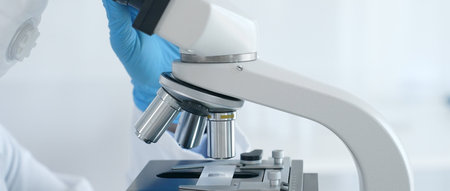 Close up of scientists hands in blue gloves adjusting microscope in laboratory, conducting...