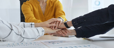 Business professionals joining hands over workplace documents, symbolizing collaborative spirit and...