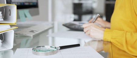 A female accountant in a yellow blouse reviews financial records and analyzes data at her office...