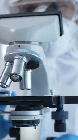 Medical virologist in a hazmat suit, mask, and gloves, diligently working at a microscope in a...