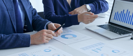 Business team analyzing financial data on a laptop and printed documents, pointing at charts and...