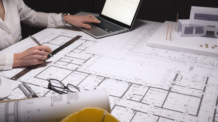 Architect carefully drawing detailed blueprints for a new construction project at a cluttered desk...