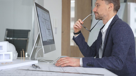 Man architect wearing glasses, is designing building plans on computer, thinking and concentrating...