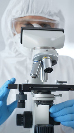 Male scientist virologist wearing hazmat suit, mask, and blue gloves, diligently working at a...
