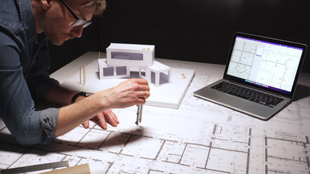 Architect drawing precise measurements and evaluating blueprints while also working on a physical...
