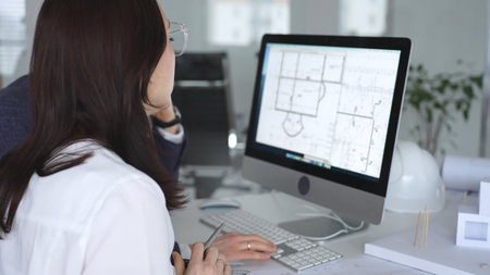 Architects collaborating on building plans using computer aided design software and architectural...