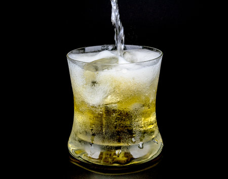 Glass and ice with whiskey on black background.の写真素材