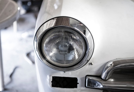 The headlight of the old car. This car is under repair. White car metal and chrome.の写真素材