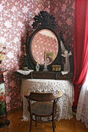 An old mirror in a frame on a table covered with a knitted tablecloth. Retro interior. Pink wallpaper with flowers. Reflection in the mirror.のeditorial素材