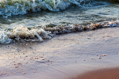 Waves on the sandy shore of a large river. The rays of light are reflected in the waves,