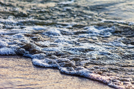 Waves on the sandy shore of a large river. The rays of light are reflected in the waves,の写真素材