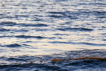 Waves on the sandy shore of a large river. The rays of light are reflected in the waves,の写真素材