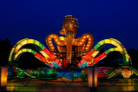 Carousel in the form of an octopus in an amusement park. Entertainment for children. Multicolored light bulbs. Evening sky.のeditorial素材