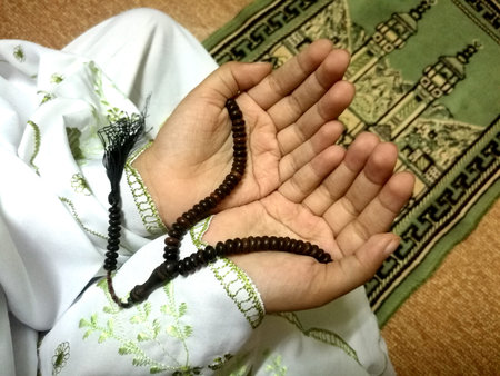 A little girl praying on the prayer mat holding tasbih beads
