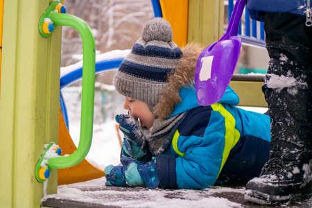 a little boy eats snow from a mitt in winterの写真素材
